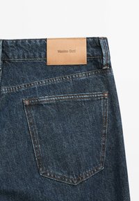 Mörkblå denimjeans med en läderetikett märkt "Massimo Dutti", med kontrasterande orange sömmar och en bakficka.