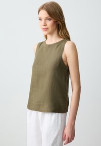 Top senza maniche verde oliva in lino texturizzato con scollo rotondo e orlo dritto, abbinato a pantaloni bianchi in lino.