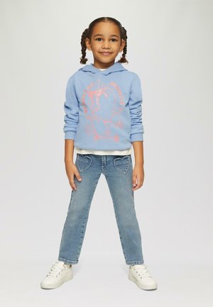 Hellblaue Kapuzenjacke mit pinkem Grafikdesign, weißer Innenauskleidung, kombiniert mit Denim-Jeans mit herzförmigen Taschen und weißen Sneakern.