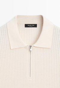 Polo in maglia a coste color crema con mezza cerniera argentata e colletto piatto, con l'etichetta del marchio Massimo Dutti visibile all'interno della scollatura.