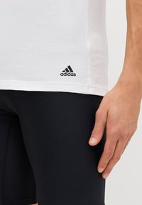T-shirt en coton blanc avec le logo Adidas noir au bas, associé à un short de sport ajusté noir. Design minimaliste, manches courtes.