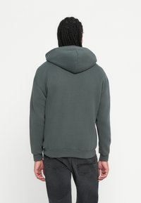 Felpa grigia realizzata in un morbido tessuto, con un ampio cappuccio e polsini a costine. Il design è semplice, senza motivi o logo visibili.