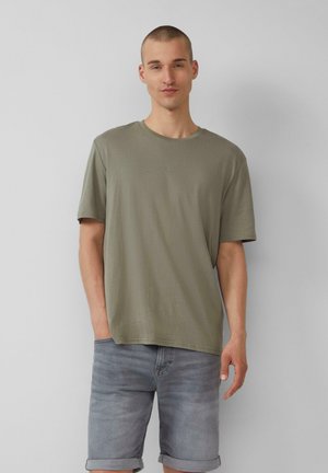 Oliwkowy t-shirt z krótkim rękawem i okrągłym dekoltem. Miękki materiał, lekko luźny krój. Zestawiony z wyblakłymi szarymi szortami dżinsowymi. Minimalne logo.