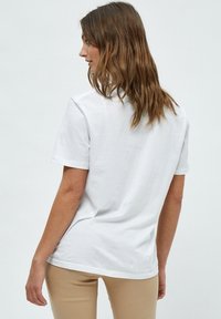 Bílý bavlněný tričko s krátkými rukávy, jednoduchý design, kulatý výstřih a volný střih, zobrazené zezadu na světlém pozadí.