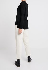 Svart långärmad topp, rund hals, sidotryck, ihopparad med off-white byxor, fransad fåll, och svarta ankelstövlar med rund tå.