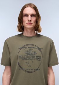 Olivengrønt bomulds T-shirt med rund hals, korte ærmer og et sort trykt logo med antarktisk grafik og tekst på forsiden.