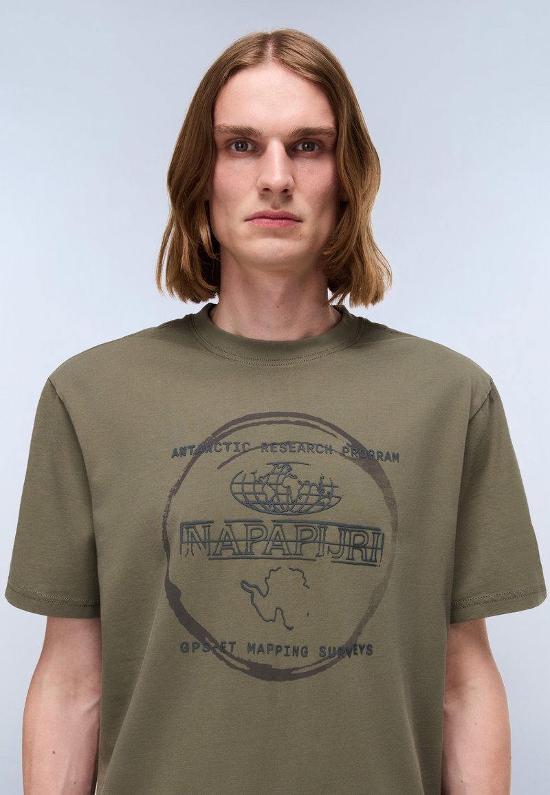 Oliwkowa bawełniana koszulka z okrągłym dekoltem, krótkimi rękawami oraz czarnym nadrukowanym logo z grafiką Antarktydy i tekstem z przodu.