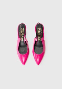 Sapatos de salto alto slingback em verniz cor de rosa, com design de bico pontiagudo, apresentando palmilhas pretas com texto dourado, textura suave e acabamento brilhante.
