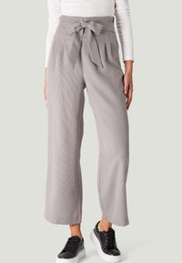 Pantalons à carreaux à jambe large en gris clair, présentant une taille haute avec un nœud. Tissu texturé, assorti à des baskets noires.