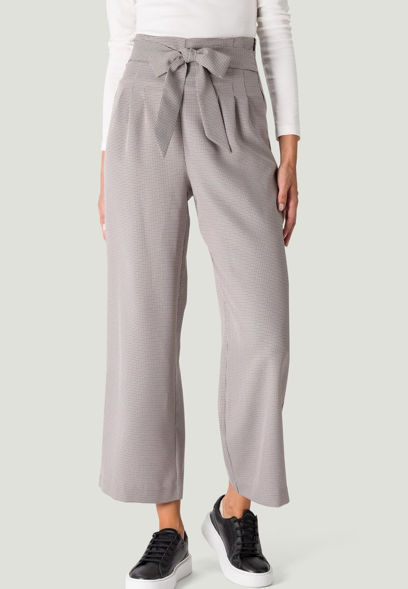 Pantalons à carreaux à jambe large en gris clair, présentant une taille haute avec un nœud. Tissu texturé, assorti à des baskets noires.