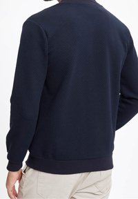 Granatowa bluza z fakturowaną powierzchnią, prążkowanym kołnierzem i mankietami oraz jednolitym obszyciem u dołu, cechująca się smukłym, casualowym designem.