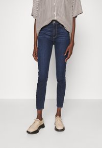 Mörkblå skinny jeans med en slät textur och subtila sömnadsdetaljer, tillsammans med ljusbeige snörskor. Ränderad skjorta ovanpå.