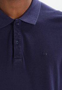 Polo bleu marine en tissu texturé avec un col, doté de deux boutons et d'un petit logo brodé sur la poitrine.