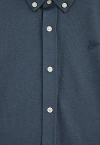 Jūras spēku polo krekls ar īsām piedurknēm, ar pogu aizdari priekšpusē un gaišām pogām, kas izceļas ar teksturētu audumu un mazu logo detaļu.