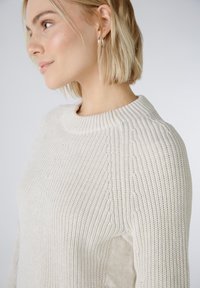 Strickpullover in hellbeige mit Rundhalsausschnitt, ausgestattet mit geripptem Muster und seitlichen Öffnungen. Weiches Material mit lockerer Passform.