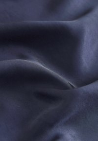 Laikuddus tume sinine kangas, millel on sujuv ja läikiv tekstuur, õrnade voltide ja kumerustega, mis demonstreerib selle paindlikku ja kerget olemust.