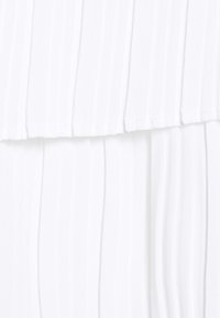 Tissu blanc avec des plis verticaux et un design en couches, montrant la texture et des plis doux dans le matériau.