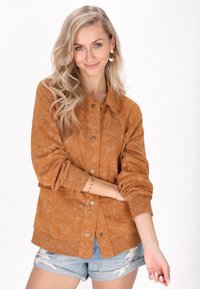 Brun, texturerad ytterjacka med knappstängning, två framfickor och ribbade manchetter, tillsammans med slitna denimshorts.