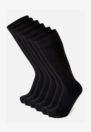 Sei paia di calzini neri in cotone con polsini a coste, texture liscia e cuciture a punta arrotondata, disposte in una fila ordinata.