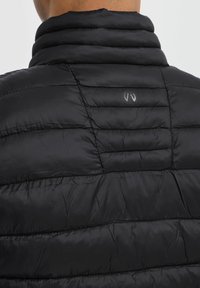 Gilet imbottito nero con texture trapuntata, colletto alto e dettaglio logo sul retro. Materiale leggero, progettato per l'isolamento.