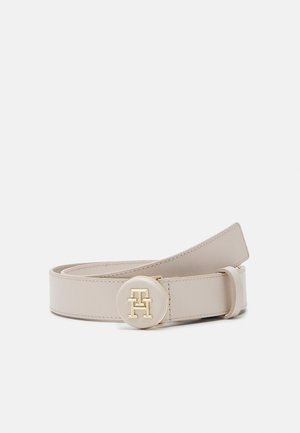 Beige leren riem met ronde gouden en beige gesp met gegraveerde in elkaar grijpende initialen, opgerold weergegeven op een witte achtergrond.