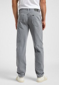 Pantaloni in denim grigi mostrati da dietro, con due tasche posteriori e un'etichetta in pelle in vita, indossati con sneakers bianche.