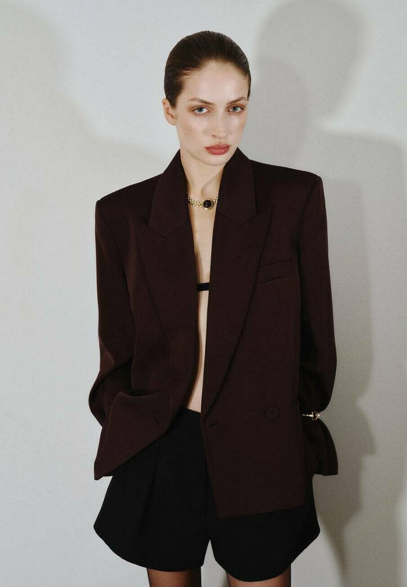 Blazer oversize color burdeos con solapas afiladas, un solo botón y bolsillos, combinado con pantalones cortos negros. Tejido suave y corte relajado.