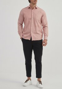 Chemise bouton de couleur rouge rayée, en mélange de coton, légère ; associée à un pantalon slim noir et des baskets blanches avec des accents marron.