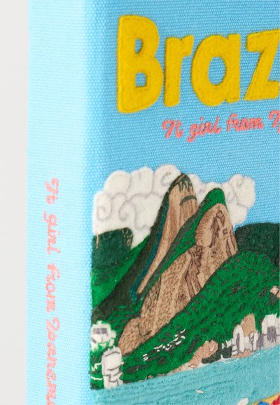 Μπλε ύφασμα στη ράχη του βιβλίου με κίτρινο κείμενο "Brazil", ροζ καλλιγραφική γραφή "It girl from" και κεντημένο τοπίο με βουνά, πράσινους λόφους και σύννεφα.