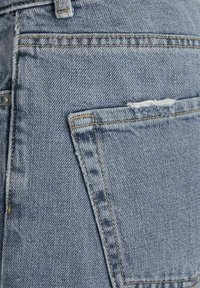Jeans de mezclilla azul claro con un bolsillo trasero con bordes deshilachados, costuras visibles y una superficie de tela texturizada.