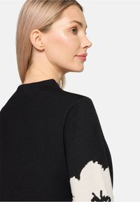 Czarny sweter z okrągłym dekoltem, z białym kwiatowym wzorem na rękawach. Miękka tekstura, dopasowany krój, minimalistyczny styl.