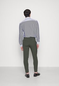 Manskjorta i blå och vita vertikala ränder, matchad med gröna slim-fit byxor. Skorna är svarta med en slät finish.