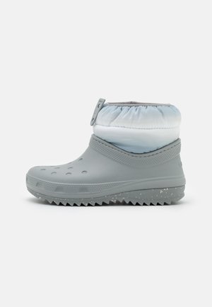 Bota cinza impermeável com sola texturizada, bico arredondado e um punho de um azul claro suave franzido no tornozelo.