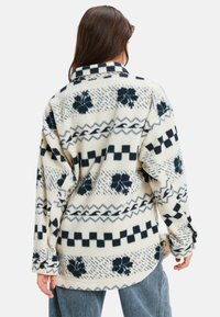Fleece shirt in crème met marineblauwe patronen, met een geruit rand en bloemaccenten. Lange mouwen, met knoopmanchetten en een relaxte pasvorm.
