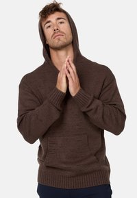 Sweat à capuche en tricot marron avec une poche avant et des poignets côtelés. Il présente une capuche et un tissu texturé avec une coupe ample.