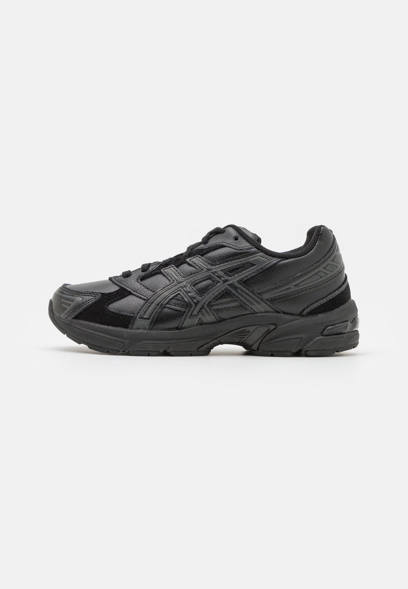 Baskets de sport noires avec fermeture à lacets, semelle texturée et détails cousus sur le côté, présentées de profil sur un fond clair.
