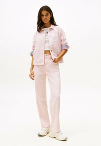 Giacca di denim rosa chiaro con maniche arrotolate, abbinata a pantaloni dritti rosa coordinate. Un top corto bianco e sneaker chiare completano l'outfit.