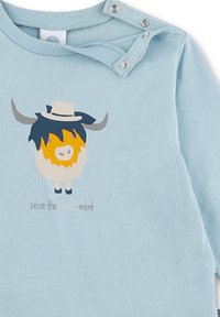 Hellblauses langärmliges Hemd mit einem cartoonhaften Highland-Rind-Grafik, das einen weißen Hut trägt, und dem Text "seize the mooo-ment" darunter. Druckknopfverschluss an der Schulter.