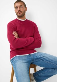 Maglione a coste con collo a giro in rosa intenso, abbinato a jeans blu chiaro. Il tessuto è strutturato, con una vestibilità morbida e un design confortevole.