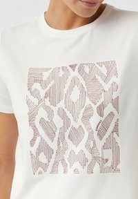 Biała koszulka z krótkim rękawem z teksturowanym abstract wzorem zwierzęcym w kolorze różowego złota na środku. Gładki, okrągły dekolt.
