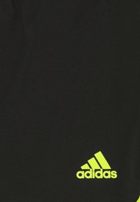 Pantalones cortos deportivos negros con un logo de Adidas en neón amarillo destacado en el lado inferior izquierdo, hechos de una tela ligera con una textura suave.