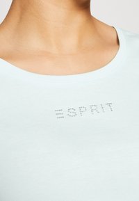 T-shirt en coton bleu clair avec un col rond et le mot "ESPRIT" en strass argentés sur la poitrine. Texture douce, design ajusté.