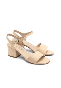 Beżowe skórzane sandały na słupku z regulowanym paskiem wokół kostki i szeroką taśmą z przodu. Lekka tekstura na górnym materiale.