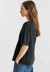 Camiseta negra de gran tamaño con mangas cortas, que presenta un cuello redondo y un corte relajado. La tela parece suave con una textura ligeramente desgastada.