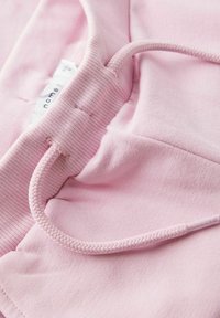 Ružićasti kaput od mekog materijala, s pletenim vezicama i rebrastim manžetama. Oznaka vidljiva unutar odjeće.