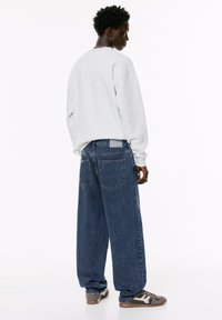 Felpa grigia oversize abbinata a jeans in denim blu a vestibilità ampia. I jeans presentano un classico design a cinque tasche e una finitura testurizzata.