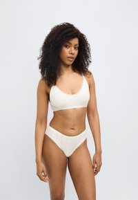 Σετ λευκής εσωρούχων από ελεφαντόδοντο με υφή, που περιλαμβάνει ένα μπραλέτο με δαντελένιες άκρες και αντίστοιχα σλιπ υψηλής μέσης από μαλακό, αεριζόμενο ύφασμα.