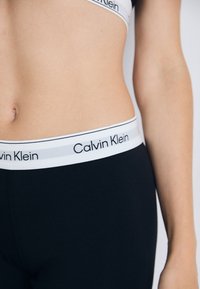Crne tajice s pojasom s logotipom Calvin Klein, koje imaju bijeli naglasak i glatku, rastezljivu tkaninu.