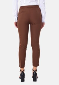 Pantaloni marroni aderenti con una superficie liscia, vita alta e una tasca posteriore singola. Indossati con sandali neri con tacco a blocco.