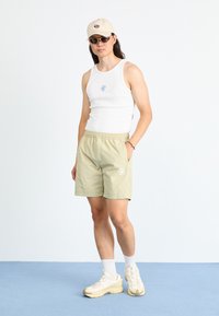 Hvit tanktop med blå grafikk, lysegrønne shorts med sidelommer og hvite detaljer, beige caps, solbriller og lyse sneakers.
